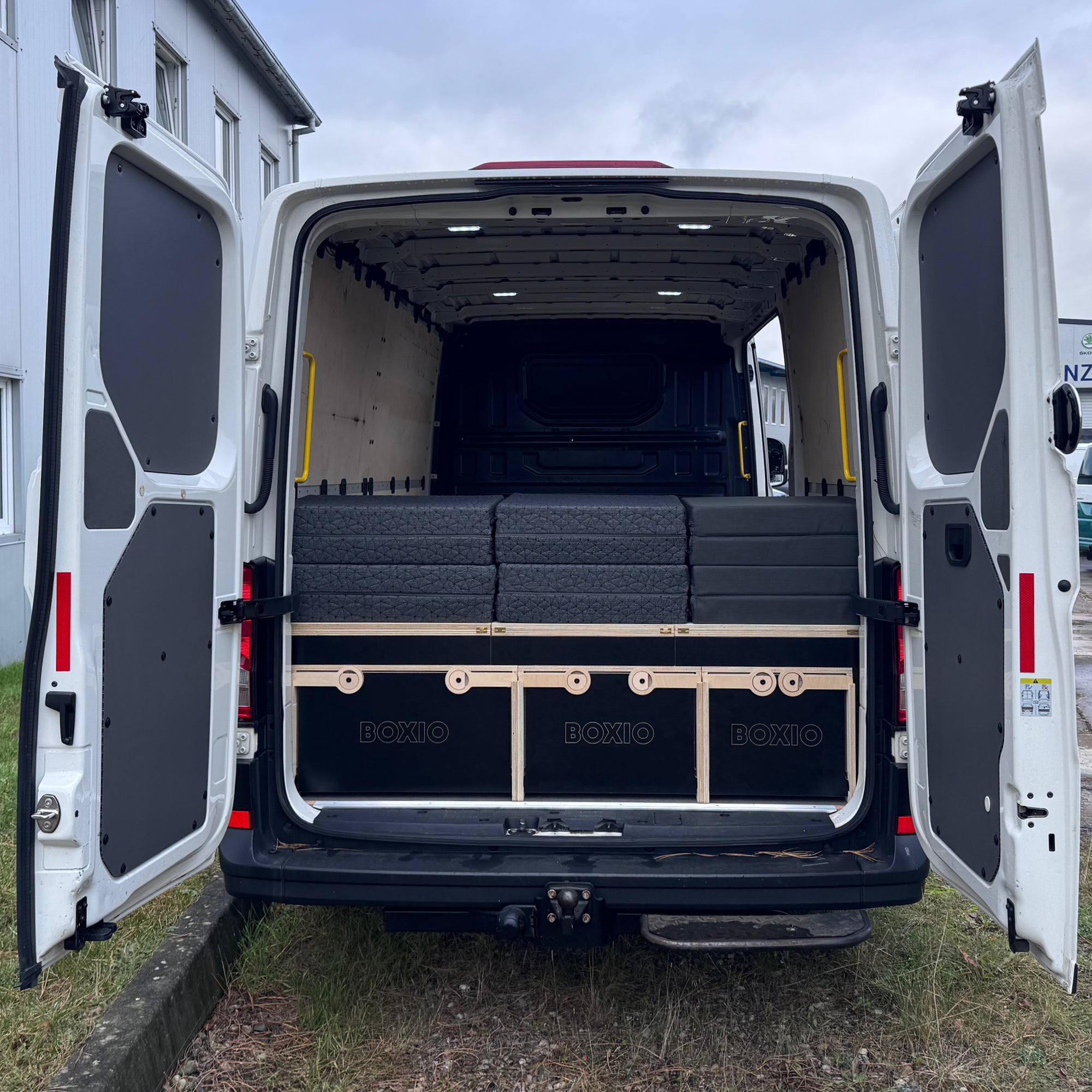 Hinteransicht eines weißen Lieferwagens mit stapelbaren schwarzen Boxen auf einer Holzkonstruktion.