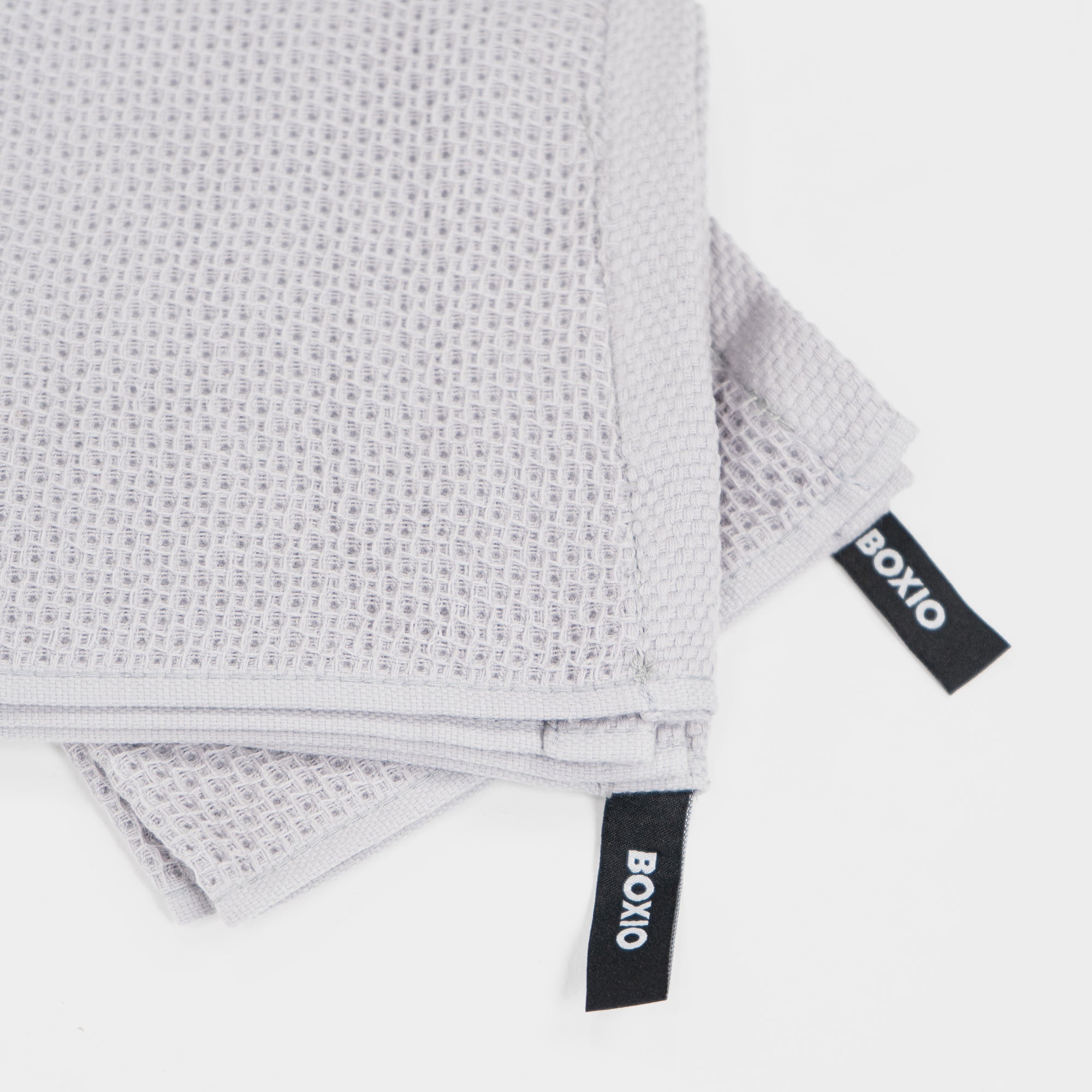 Grau gewellte Handtücher mit Labels, aus strapazierfähigem Material, übereinanderliegend auf weißem Hintergrund.