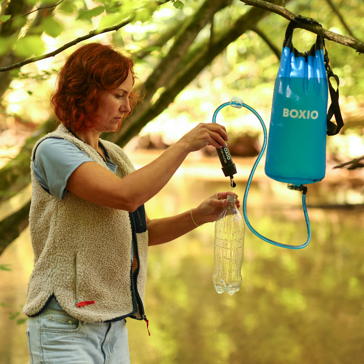 Frau füllt eine Wasserflasche mit einem Filter aus einem blauen Wasserbehälter in der Natur.