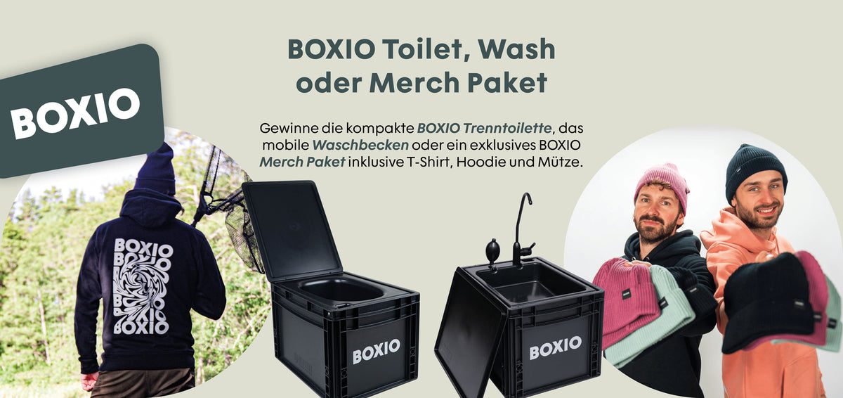Zwei Männer präsentieren verschiedene Mützen, neben ihnen stehen eine mobile Trenntoilette und ein Waschbecken von BOXIO.