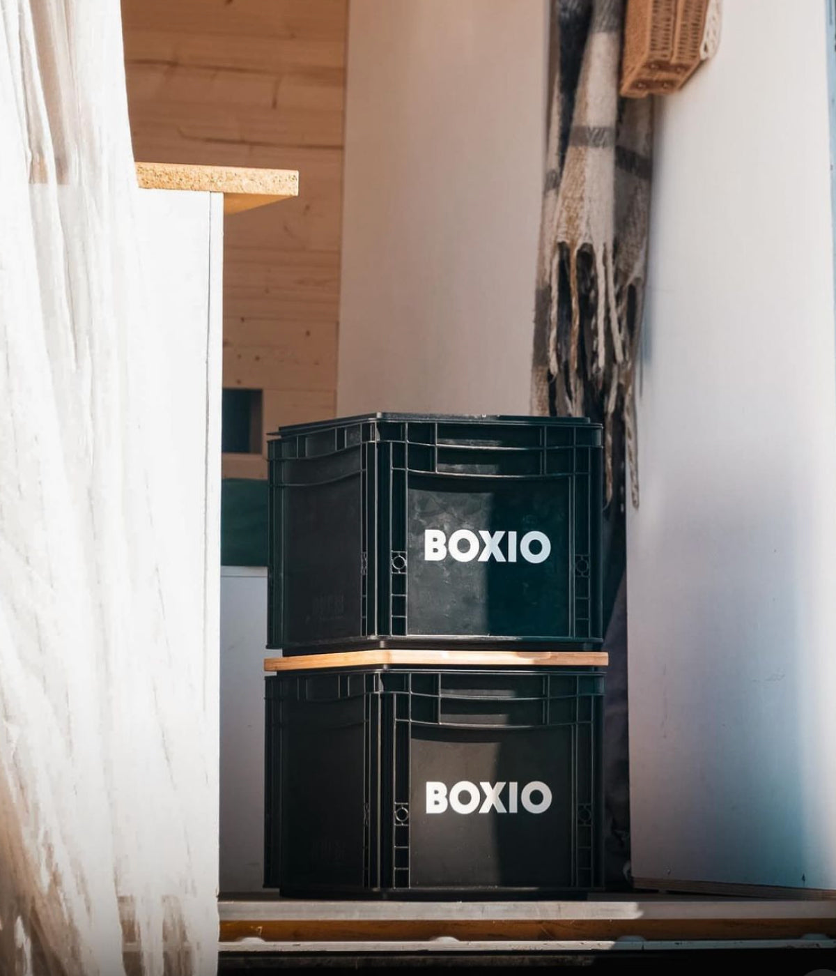 Schwarze Kunststoffboxen mit der Aufschrift "BOXIO" stehen übereinander in einem modernen Raum.