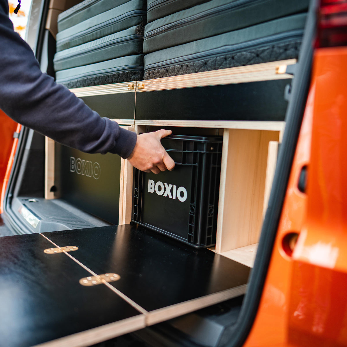 Eine Person entnimmt eine schwarze BOXIO-Box aus einem Transporter mit einem stilvollen Innenausbau.
