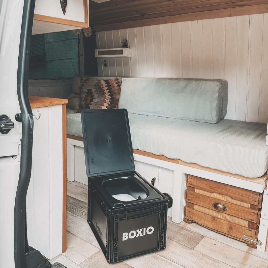 Kompakte Camper-Innenansicht mit gemütlicher Couch und schwarzem Toilettenbehälter namens BOXIO.