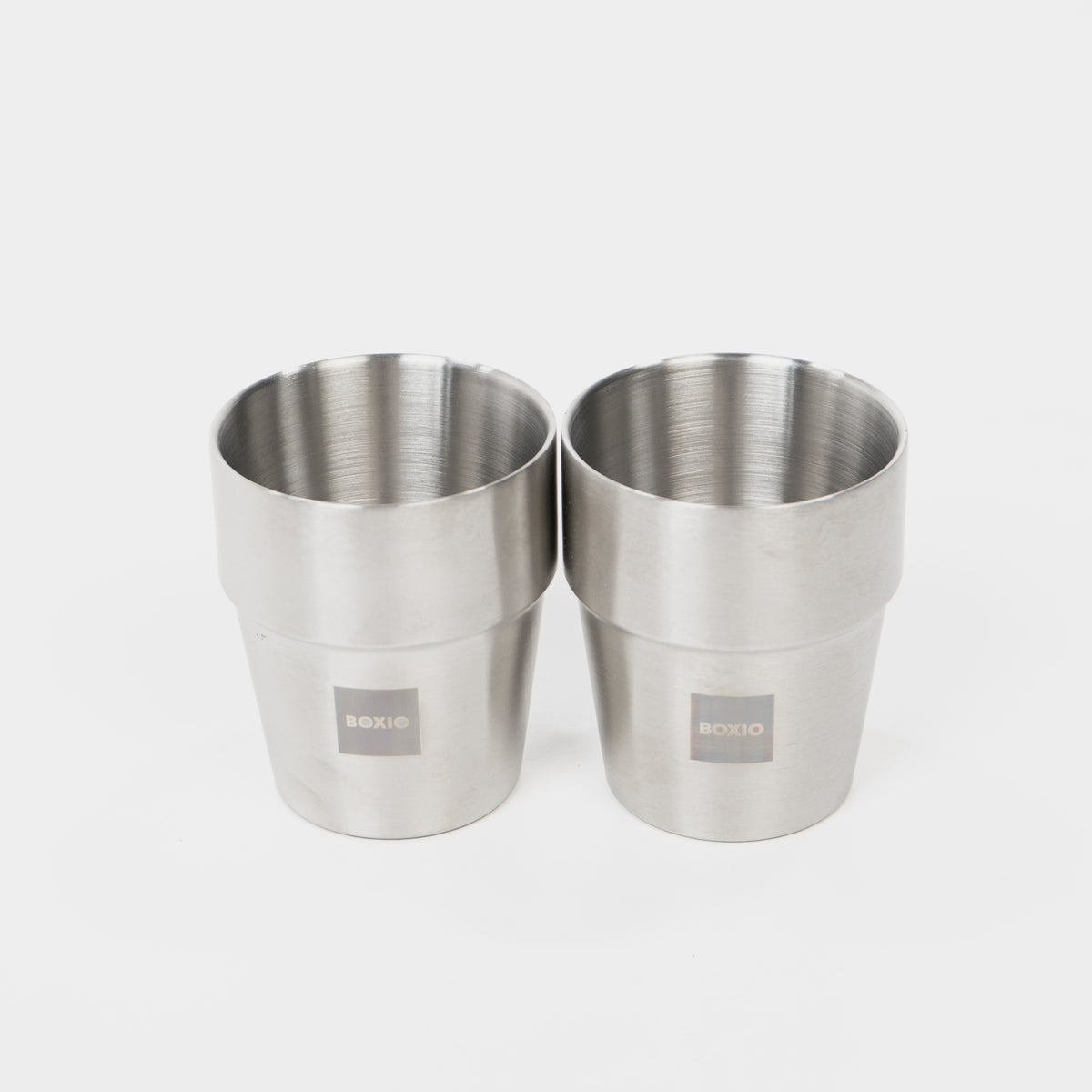 Zwei Edelstahlbecher mit leicht konischer Form und BOXIO-Logo auf der Vorderseite.