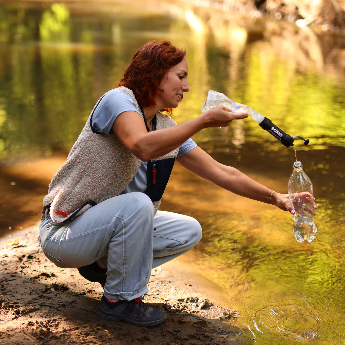 Frau füllt eine Wasserflasche mithilfe eines Filters aus einem natürlichen Gewässer am Ufer.