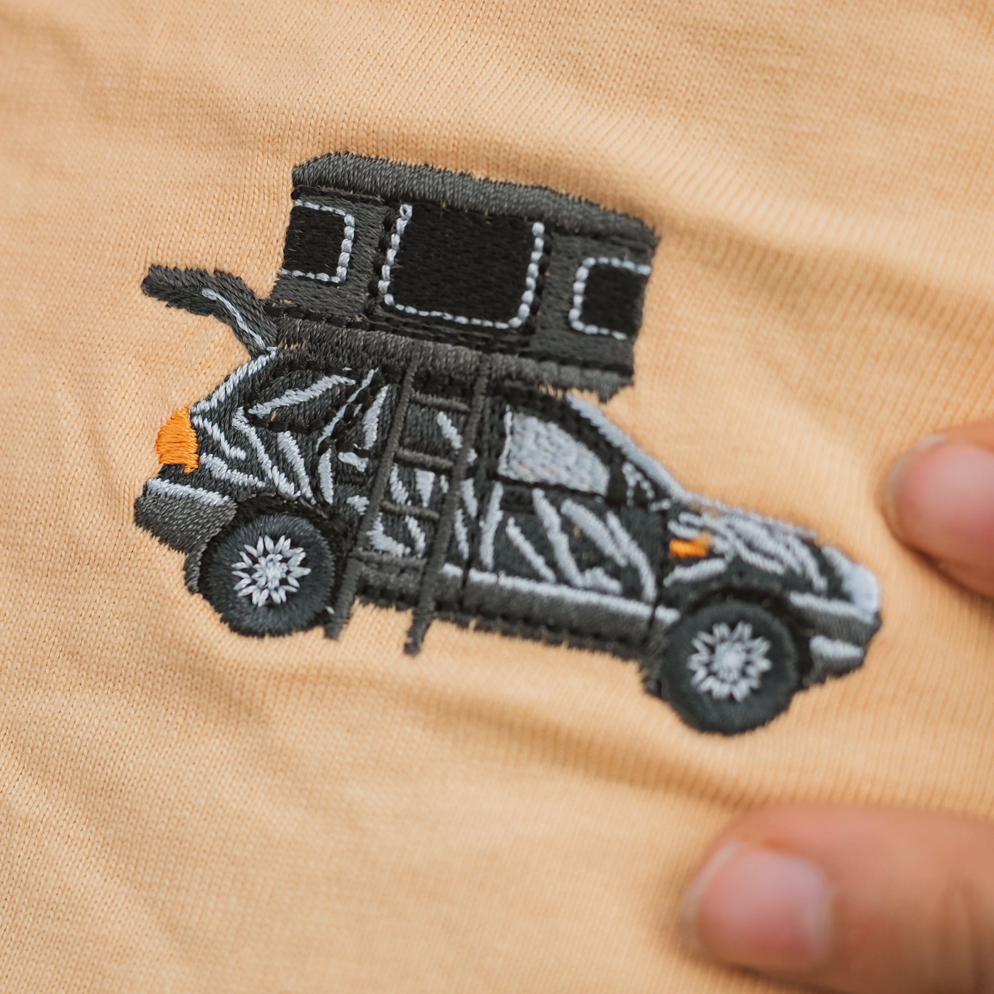 Gesticktes Motiv eines Autos mit Dachzelt auf einem beige-farbenen Stoff.