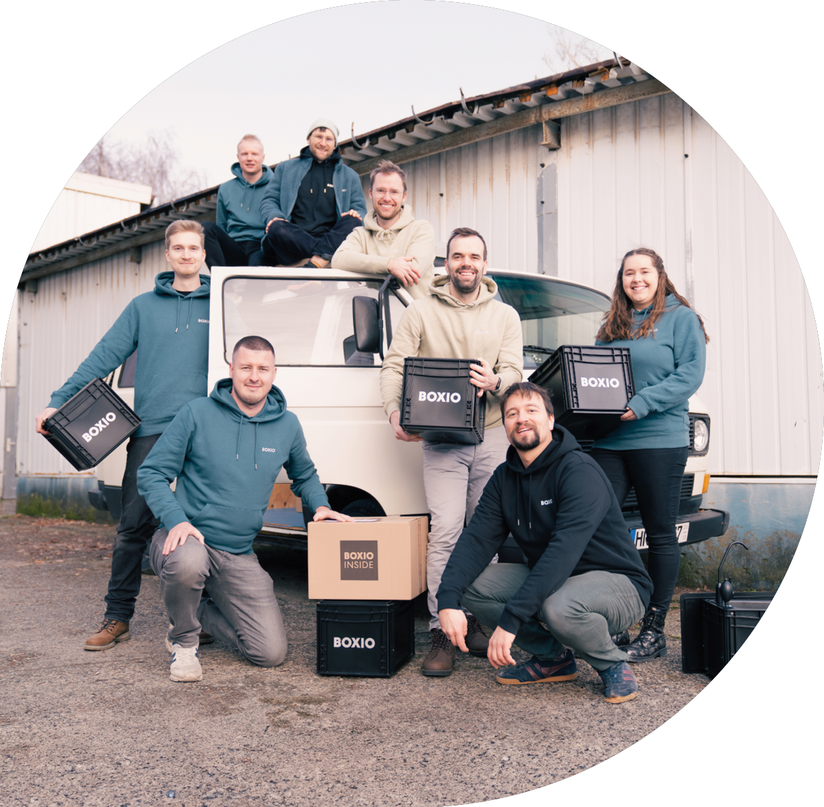 Teammitglieder von BOXIO posieren vor einem weißen Transporter, umgeben von schwarzen und braunen Kisten.