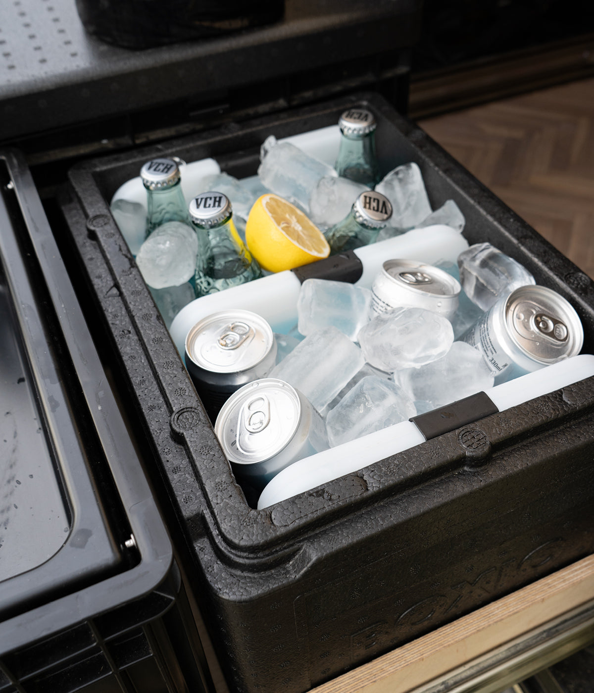Kühlbox mit Flaschen, Dosen und Eiswürfeln, dekoriert mit einer Zitronenscheibe.