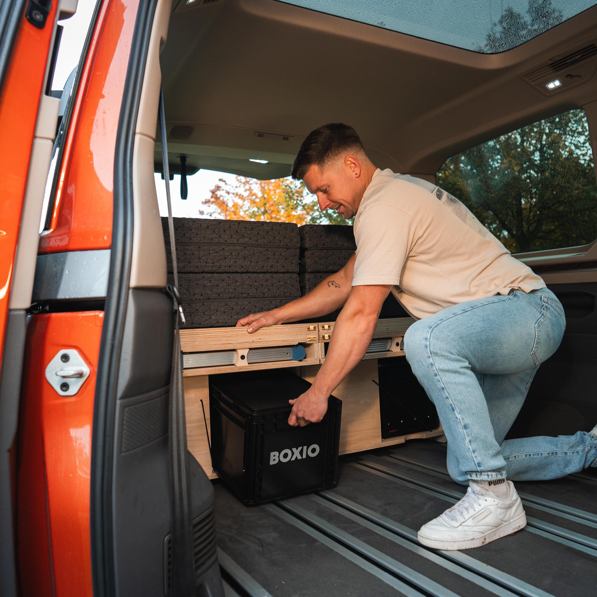 Mann im Fahrzeug lädt eine schwarze BOXIO-Box in ein maßgeschneidertes Holz-Regalsystem für Campingzwecke.
