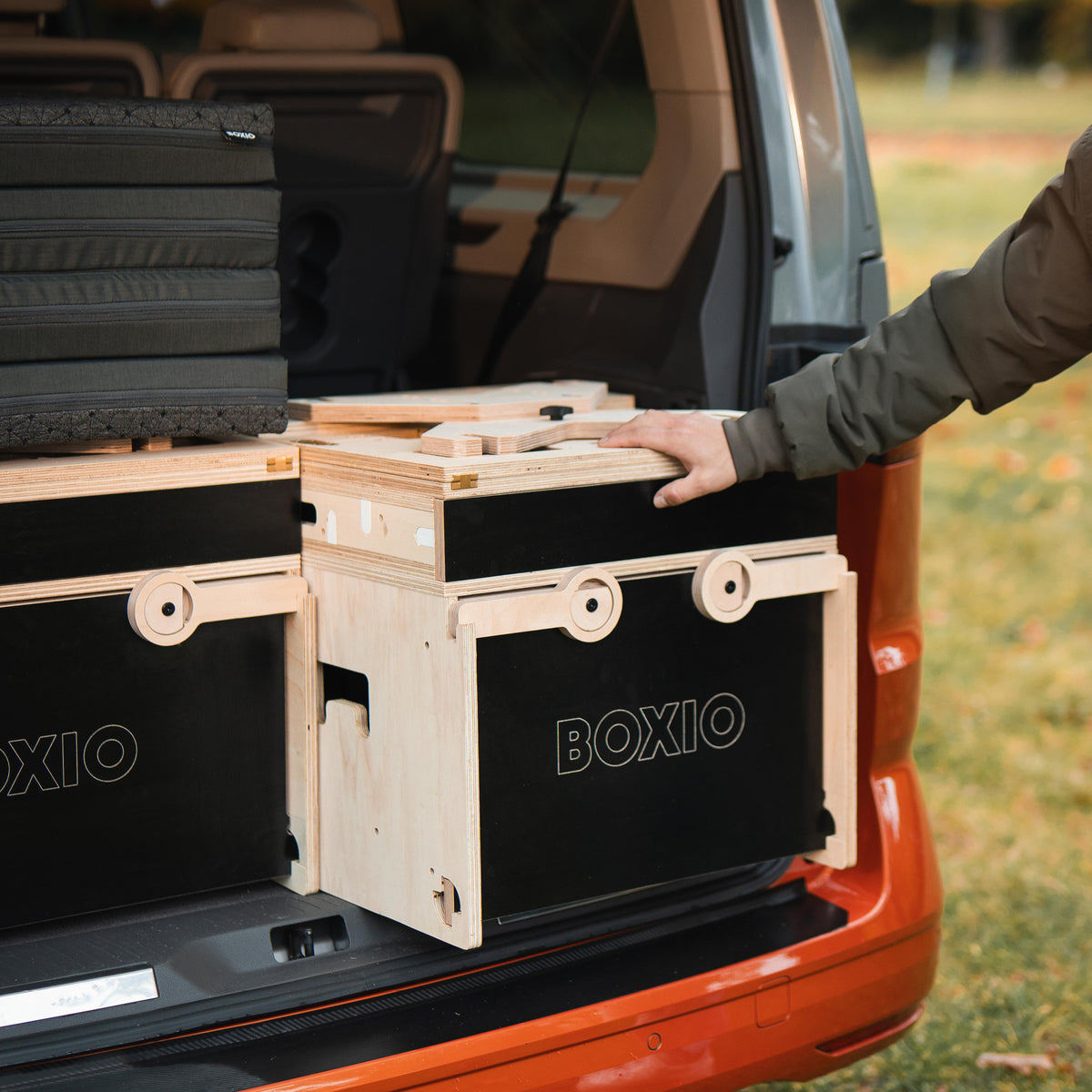 Aufgeräumter Kofferraum eines Fahrzeugs mit mehreren stabilen Boxen von BOXIO und einem gepolsterten Element.
