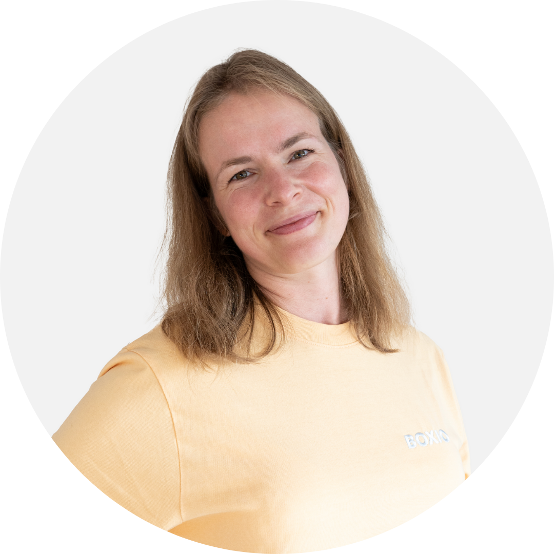 Lächelnde Frau mit langen, glatt Haaren in einem gelben Shirt, vor hellem Hintergrund.
